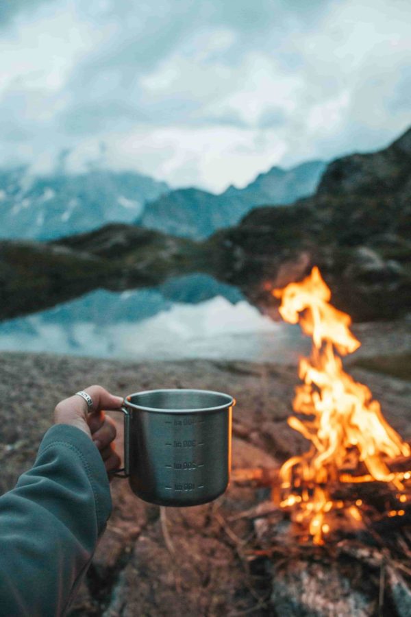 person holding mug in front of campfire and mountains